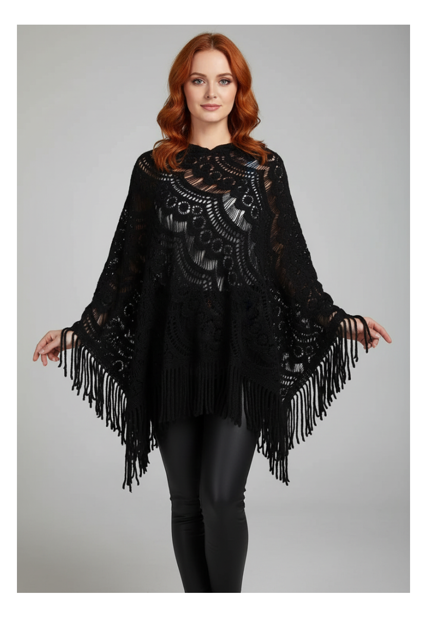 A woman with red hair wearing a black lace and fringe poncho sweater over black leggings, standing against a light gray studio background.